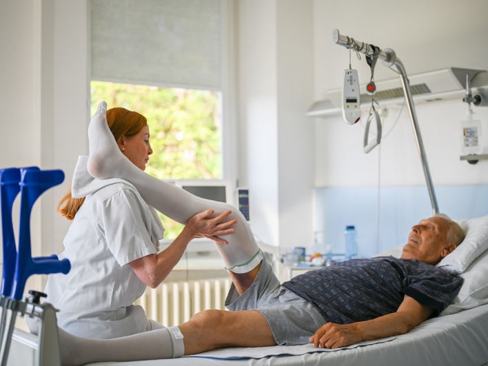 Älterer Mann im Bett mit bandagiertem Bein bei Physiotherapie