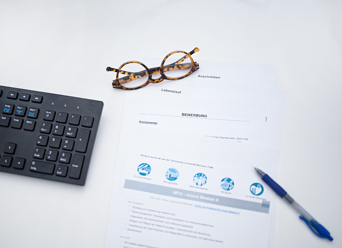 Bewerbungsunterlagen liegen neben einer Tastatur und Brille