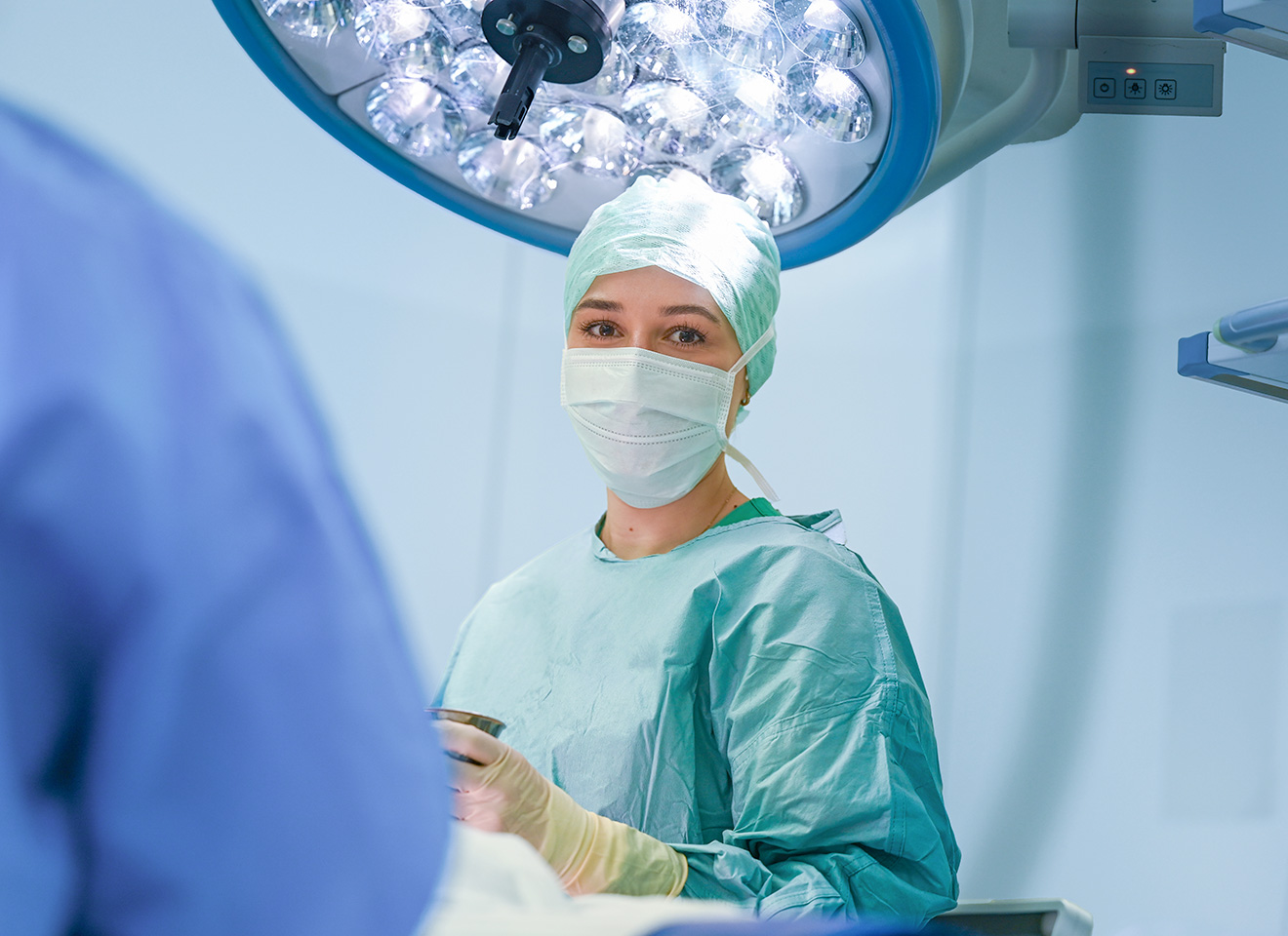 Operationstechnische Assistentin blickt während einer OP in die Kamera
