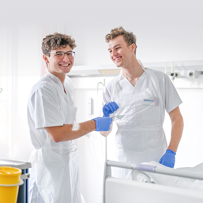 Zwei Pflegeazubis blicken während ihrer Arbeit in die Kamera
